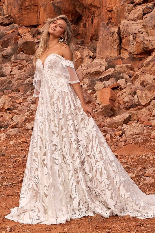 Különleges hímzett csipkével díszített A vonalú menyasszonyi ruha mély - tüllbetéttel kombinált -szív alakú kivágással. Érdekessége a bő, levehető csipkeujj, mely bohém külsőt kölcsönöz a modellnek. Egy igazán rendkívüli darab az Evie Young esküvői ruha kollekcióból! Style: Wyatt. Image fotó