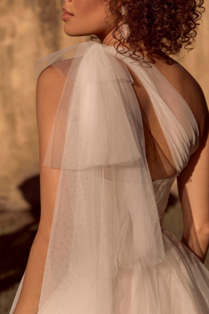 Romantikus, fodros tüll menyasszonyi ruha modern hercegnőknek, flitterekkel díszített csipkebodyval és félvállas tüll kiegészítővel a Madi Lane 2021 évi menyasszonyi ruha kollekcióból. Style: Bella. Hátulról közelről fotózva