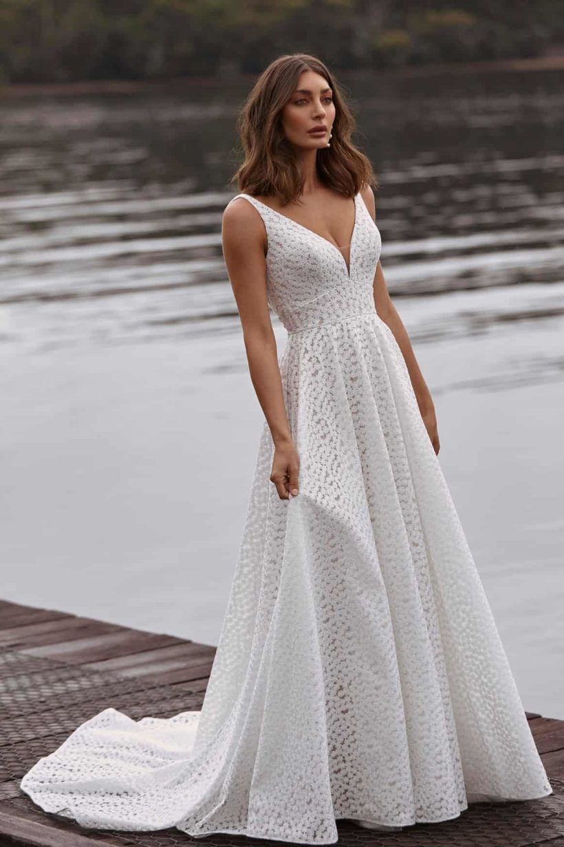 Minimalista stíusú, A vonalú, szolídan elegáns menyasszonyi ruha apró virág mintájú csipkéből. Style: Madi Lane "Clara". Elölről fotózva