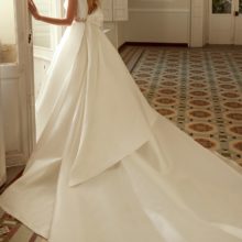 Klasszikus elegancia. Elegáns és visszafogott mikádó esküvői ruha hercegnős szoknyával és halter nyakkal. A ruha különlegessége a hátul a deréknél elhelyezett hatalmas masni. Style: Higar Novias "Enebro". Hátulról fotózva