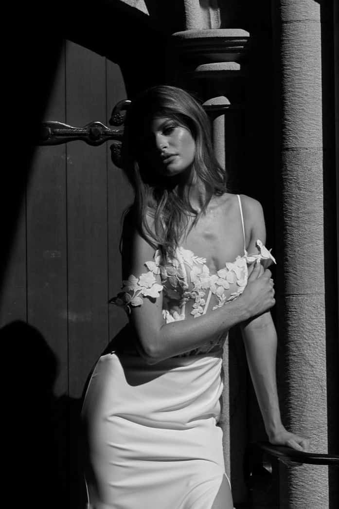 Modern, elegáns, egyszerű sellő menyasszonyi ruha csipke bodyval, magasan sliccelt szoknyával, spagettpánttal és ejtett karpánttal. Style: Evie Young "Lexi". Fekete-fehér fotó