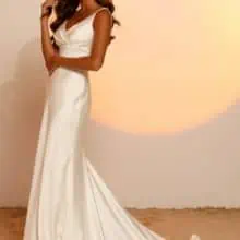 A vonalu, vállpántos V nyakkivágású lágy selyem menyasszonyi ruha mutatós uszállyal és széles övvel a derekán. Style: Jaxon a Madi Lane 2023 évi "Oasis" kollekcióból oldalról