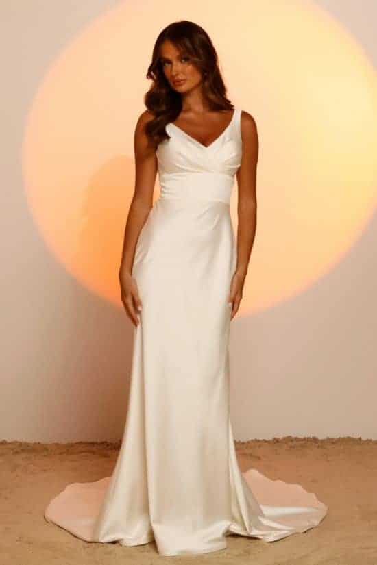 A vonalu, vállpántos V nyakkivágású lágy selyem menyasszonyi ruha mutatós uszállyal és széles övvel a derekán. Style: Jaxon a Madi Lane 2023 évi "Oasis" kollekcióból. Elölről