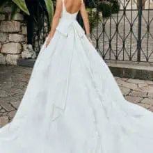 Sima, egyszerű esküvői ruha brokát anyagból. Bodyja szolíd kivágású, széles vállpántú, a ruha hátuját pedig masni díszíti. Style: Veni Infantino "52075" Hátulról fotózva