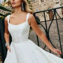 Sima, egyszerű esküvői ruha brokát anyagból. Bodyja szolíd kivágású, széles vállpántú, a ruha hátuját pedig masni díszíti. Style: Veni Infantino "52075" Közelről fotózva